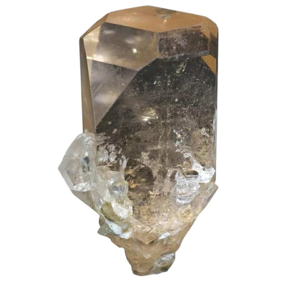 A brilliant transparent light brown topaz crystal with minerals attached to it at the bottom