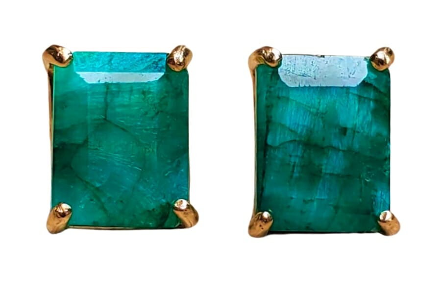 A pair of golden stud earrings adorned by bluish-green emeralds