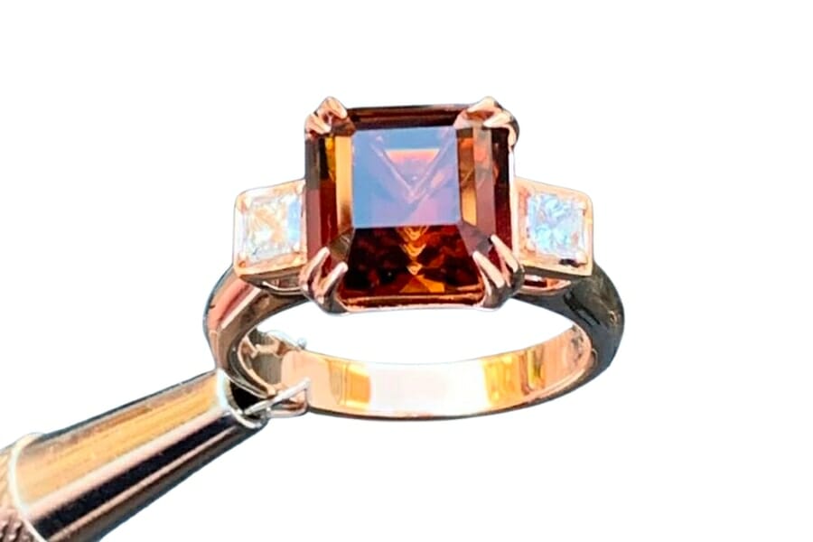 A gold ring with a sherry topaz set as center stone held by a jewelry plier