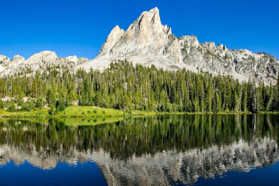 The majestic formation of the Sawtooth Mountains with a line of lush green trees and clear lake water at its foot