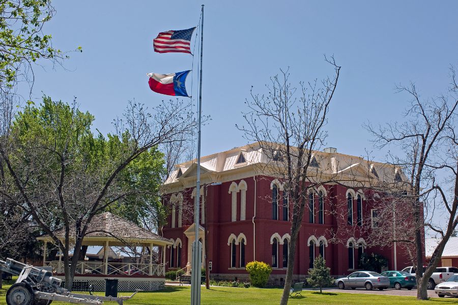 red brick building with the American flag an Texas state flag on a pole