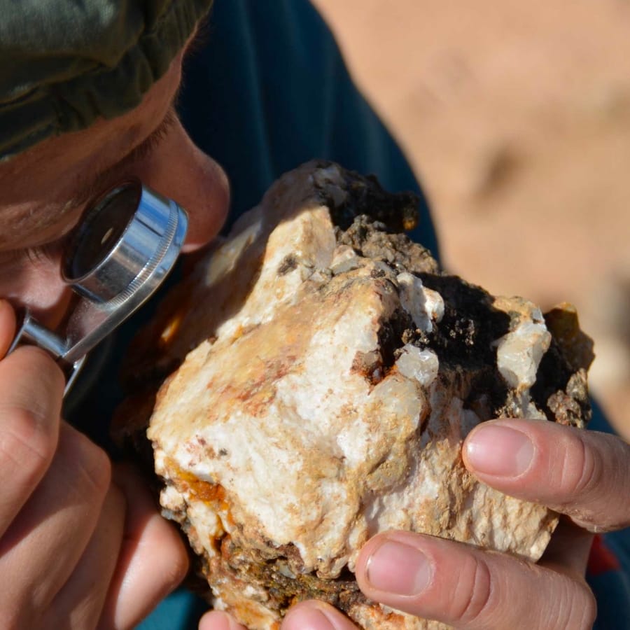 A man closely inspecting a specimen using a magnifying glass