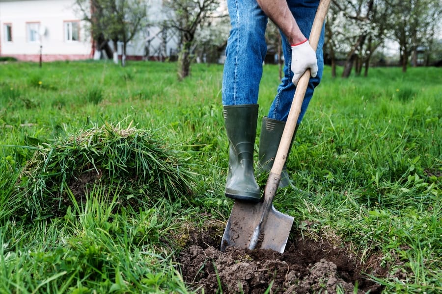 A man digging a hole on a grassland using a shovel