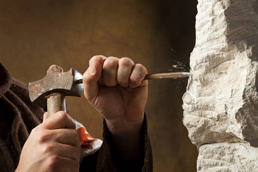A person using a hammer and chisel to break down a rock