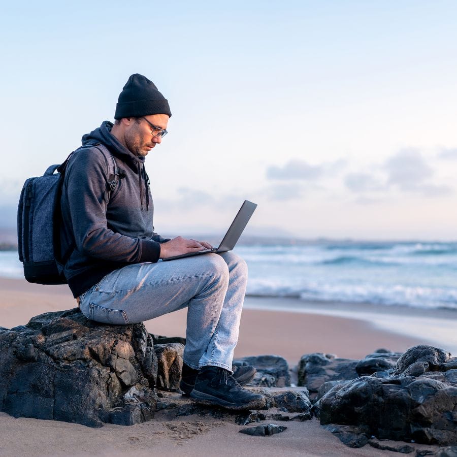 man sitting on a rocky beach with a laptop