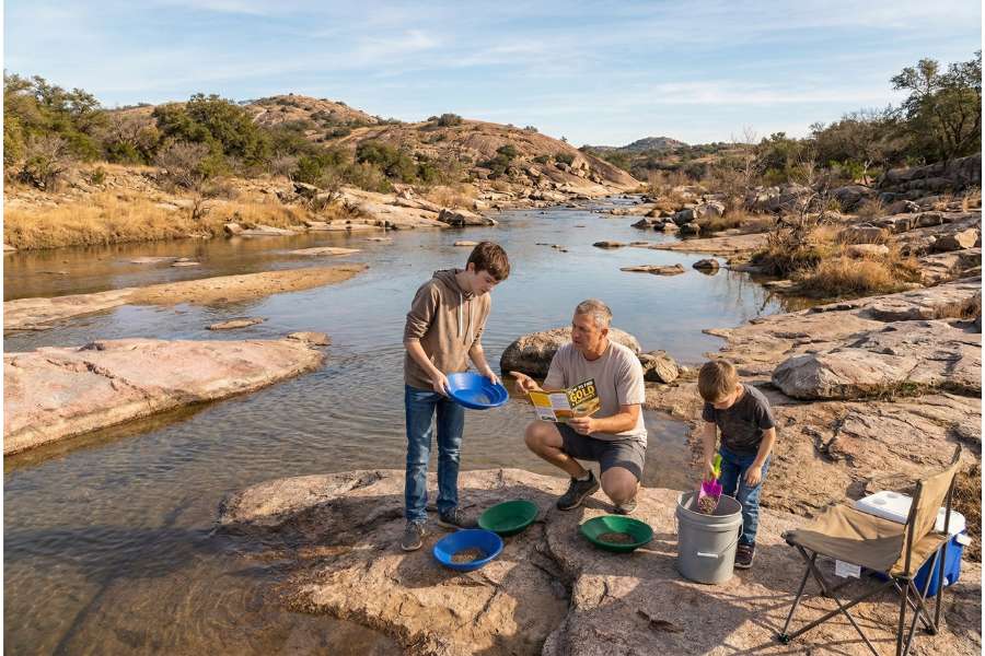 My father and two children digging through the rocks in a river looking for gold